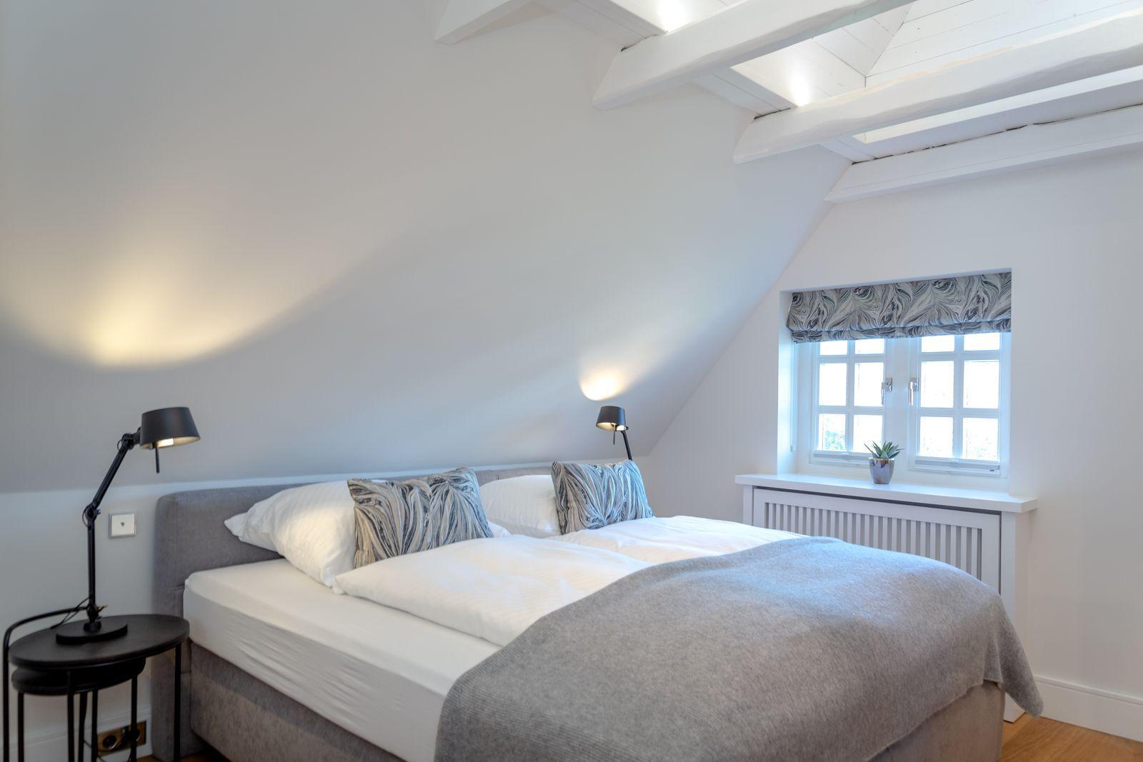 Bedroom with double bed, window, and wooden beams on the ceiling.