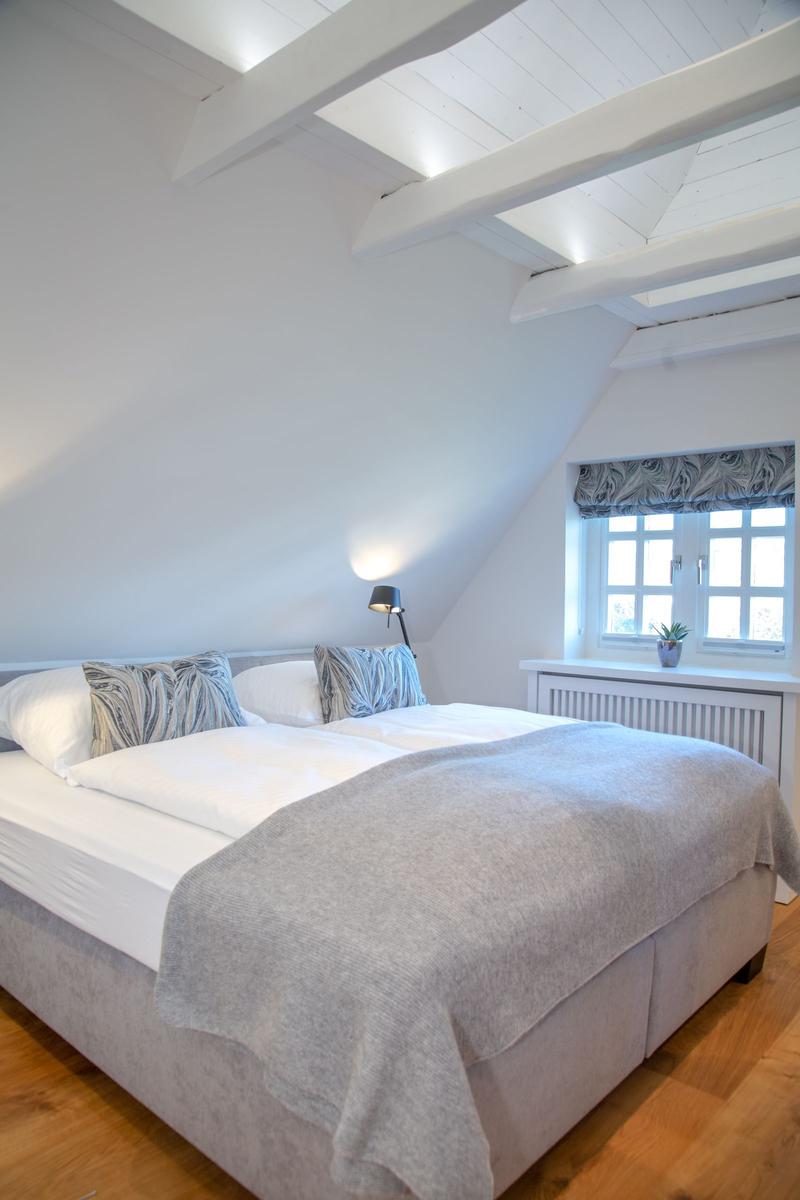 Bedroom with double bed, wooden floor, and sloped ceiling beams. Window with curtain.