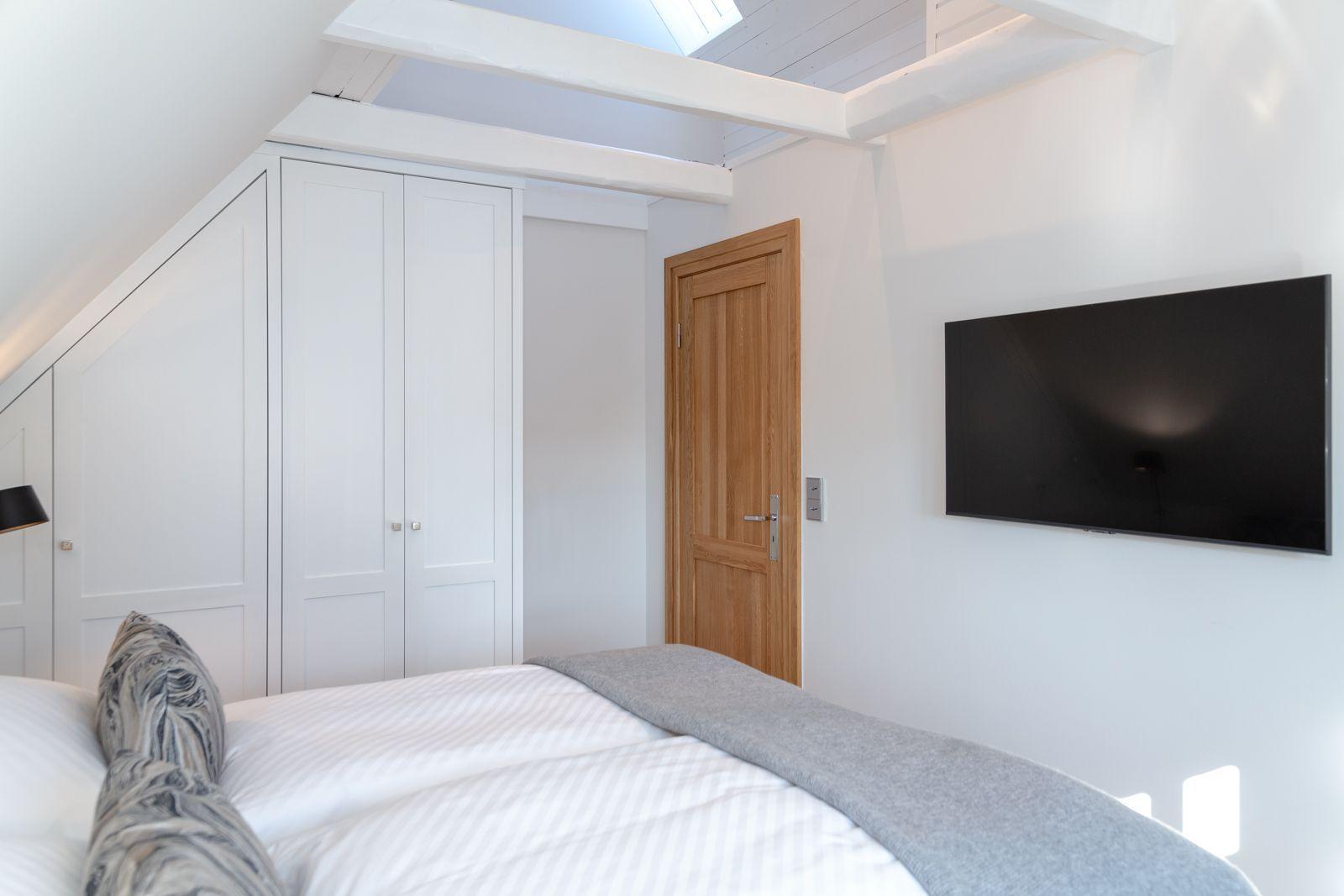 Bedroom with bed, wardrobe, and wall-mounted TV under sloped ceiling.