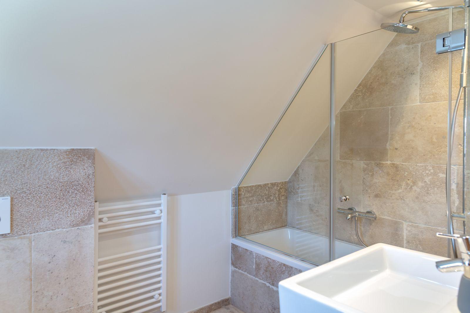 Bathroom with shower, sink, and heater under sloped ceiling