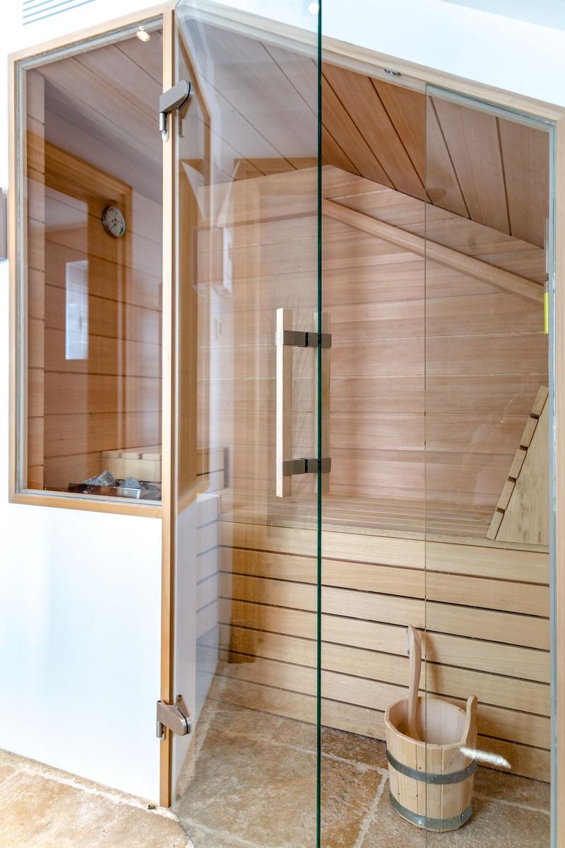 Sauna with wooden walls and glass door, wooden bench and bucket with ladle