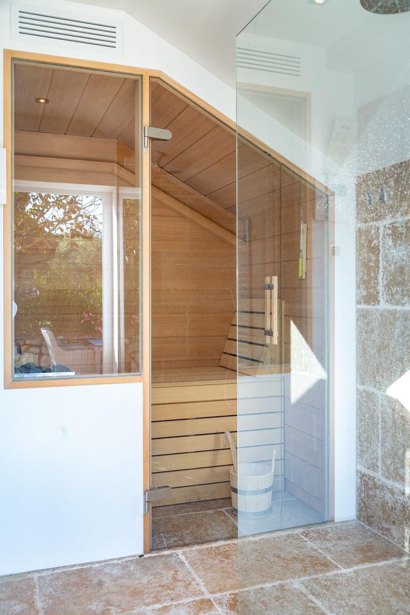 Sauna with wooden walls and bench, separated by glass wall.