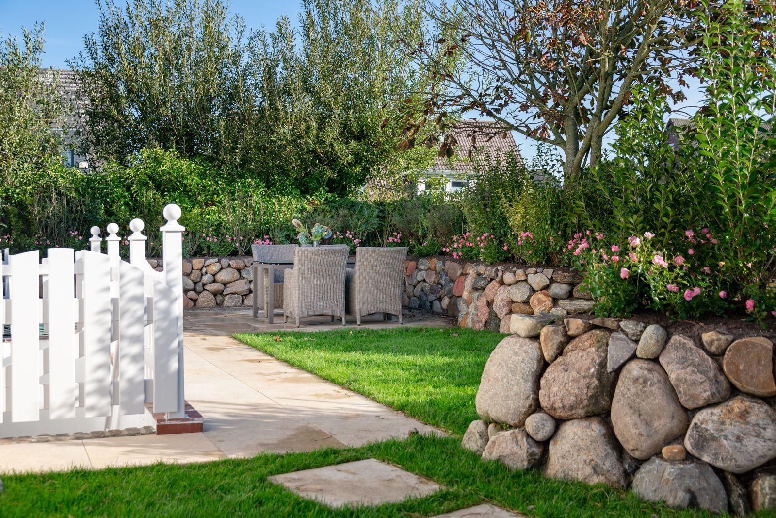 Backyard with white fence, stone wall, and seating area in garden.