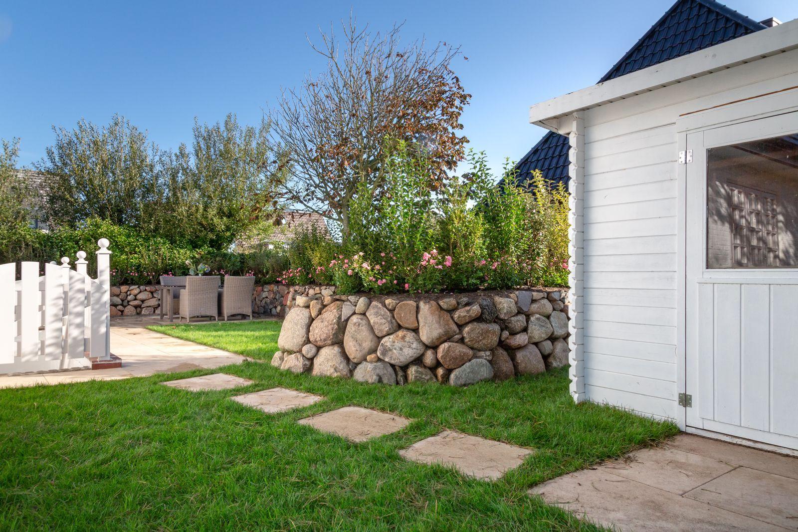 Backyard with stone wall, flower bed, and white wooden shed