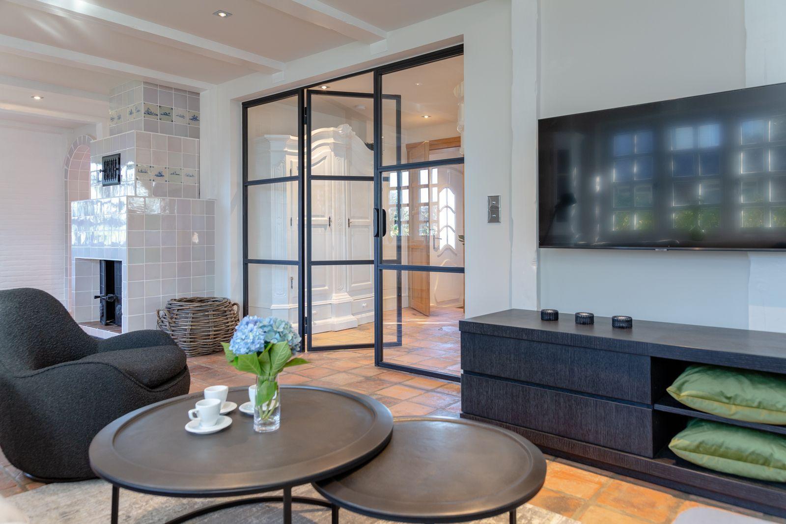 Living room with fireplace, glass doors, and TV. Round tables and seating area.