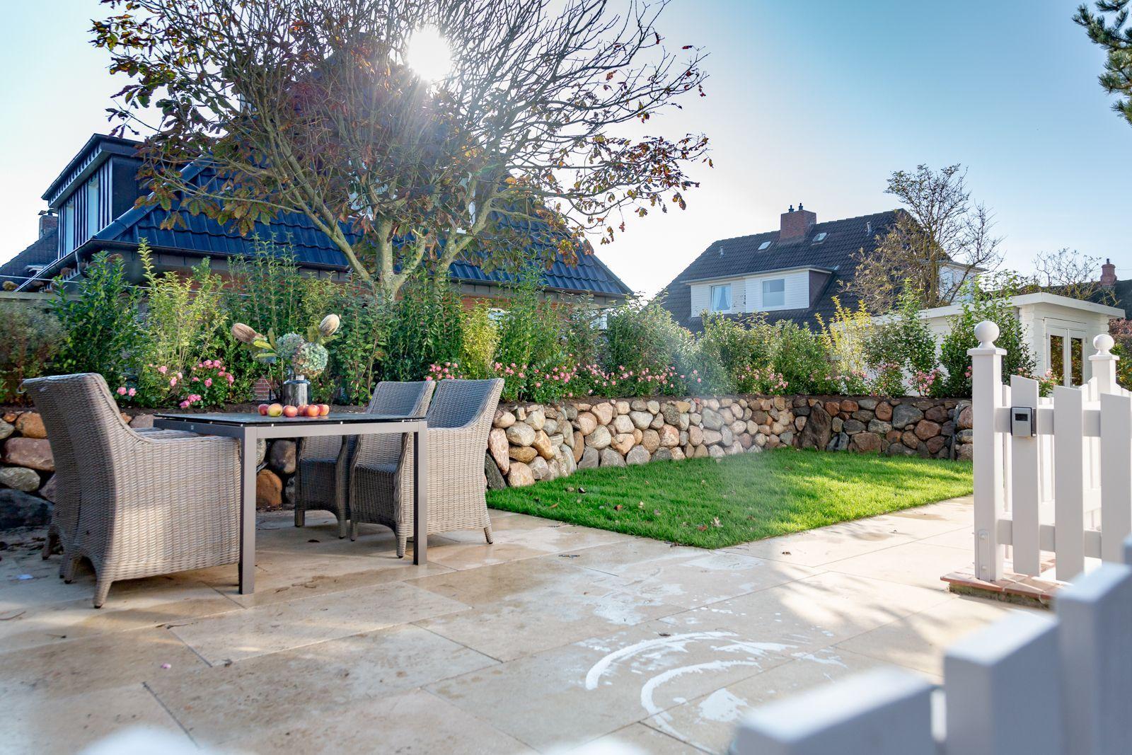 Terrace with garden, table and chairs. Backyard with stone wall and grass.