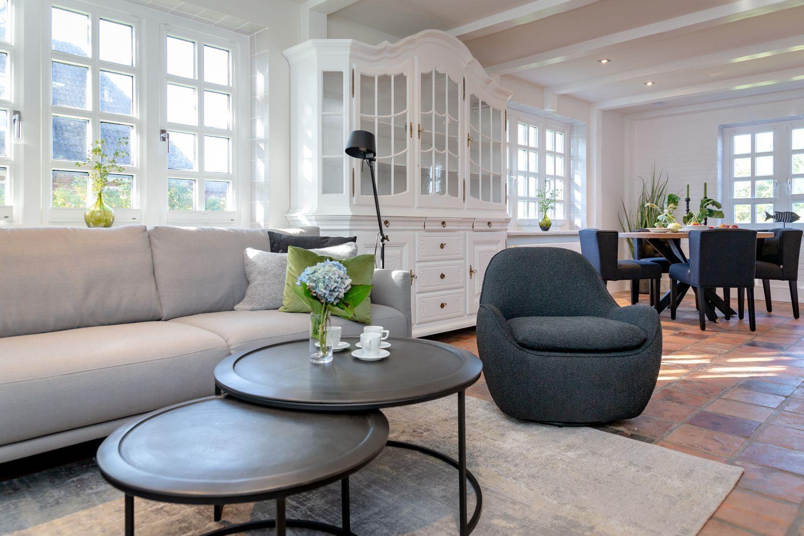 Living room with sofa, armchair, and dining table. Terracotta floor and white cabinet.