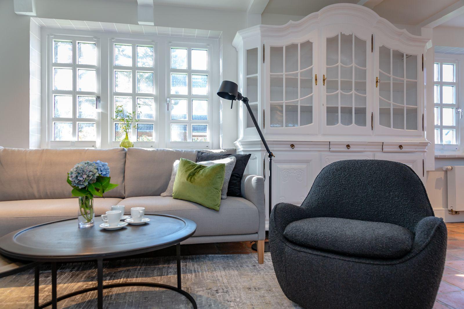A living room with sofa, armchair, table, and windows.