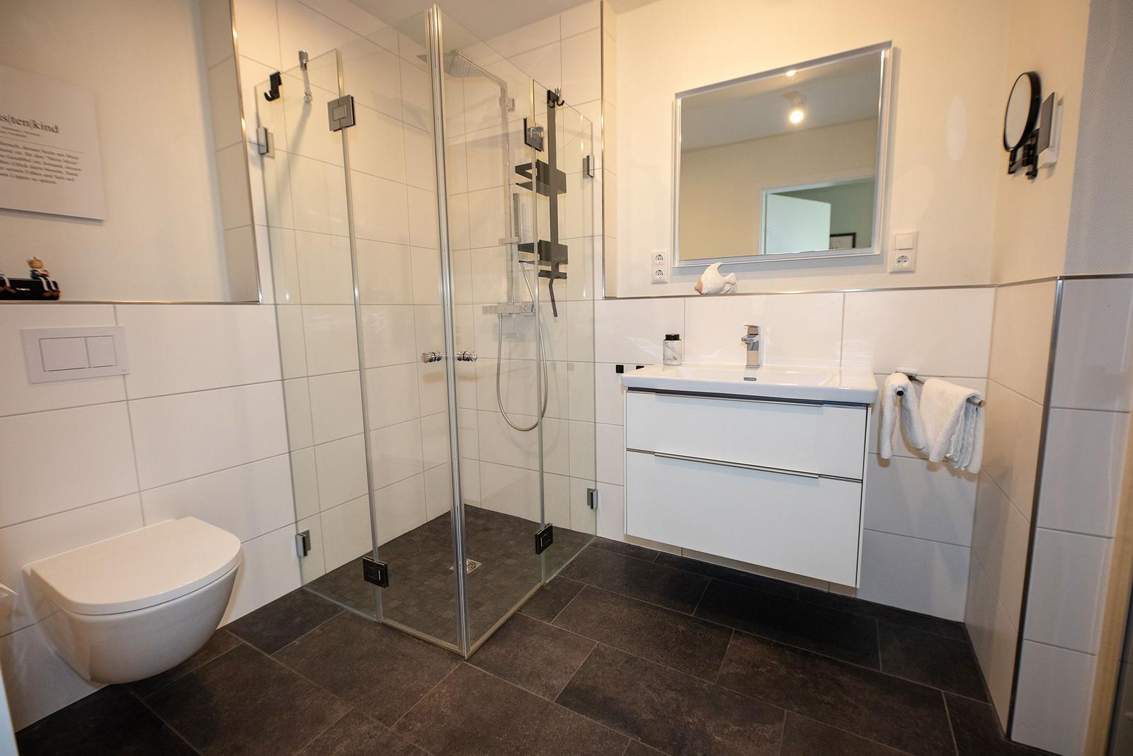 Badezimmer mit Dusche, Waschbecken und Toilette. Fliesenboden und Spiegelschrank.