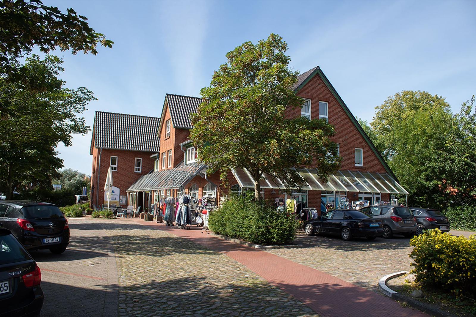 Rotes Backsteingebäude mit Glasdach und Parkplatz. Bäume und gepflasterte Wege.