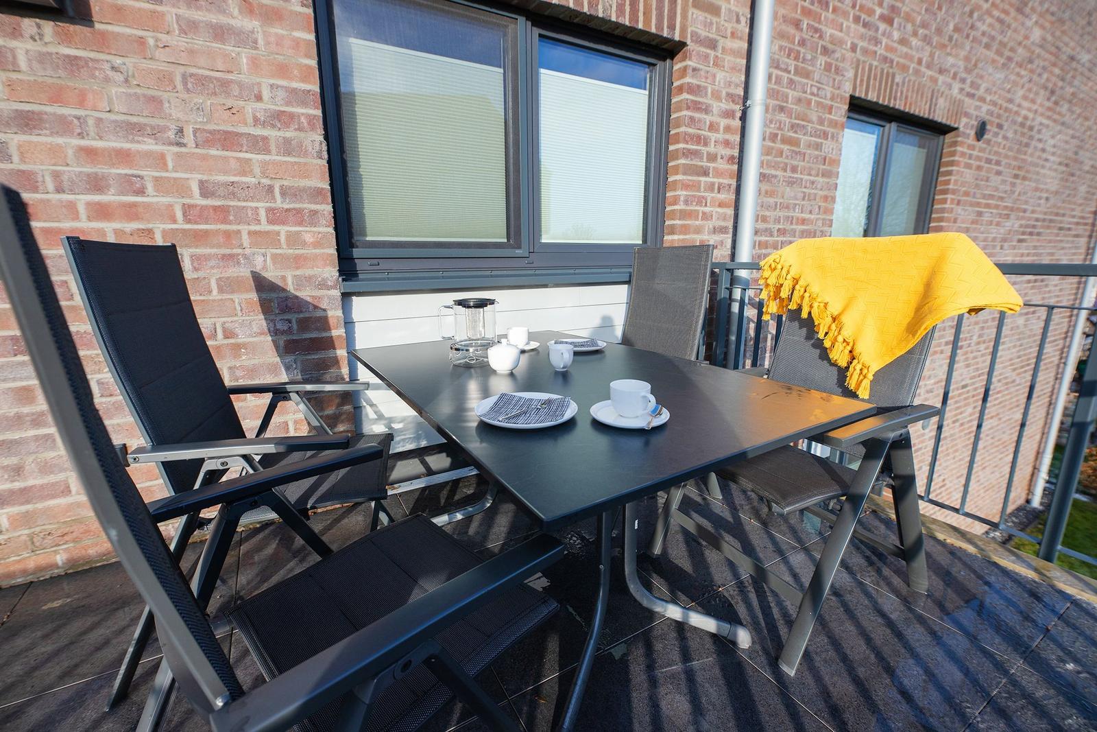 Terrasse mit Tisch, Stühlen und gelber Decke vor Backsteinhaus