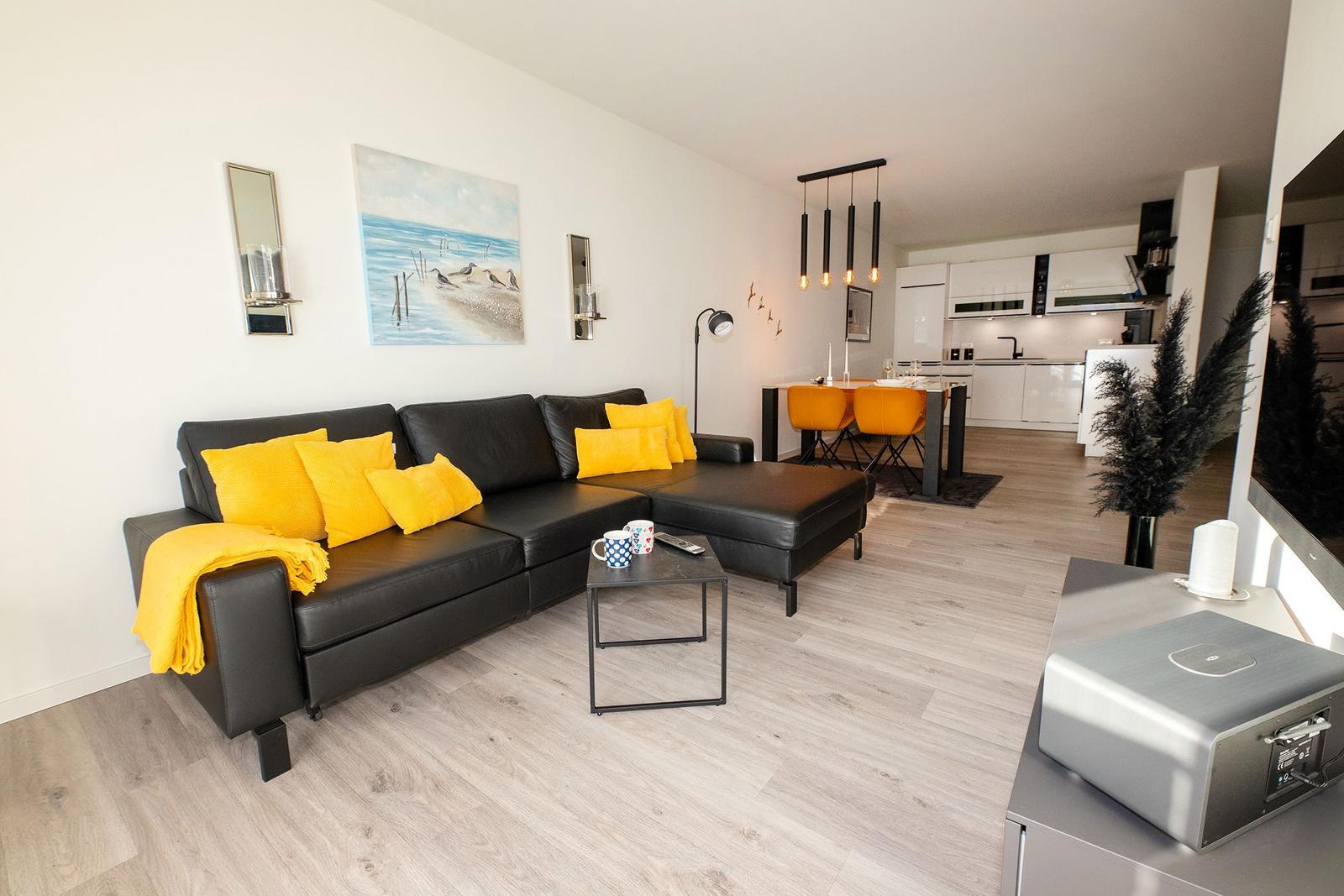 Schwarzes Sofa mit gelben Kissen, Essbereich und Küche im Hintergrund.
