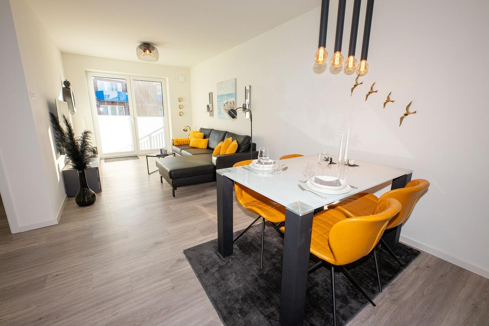 Essbereich mit gelben Stühlen und Esstisch. Wohnbereich mit Sofa und Terrassentür.