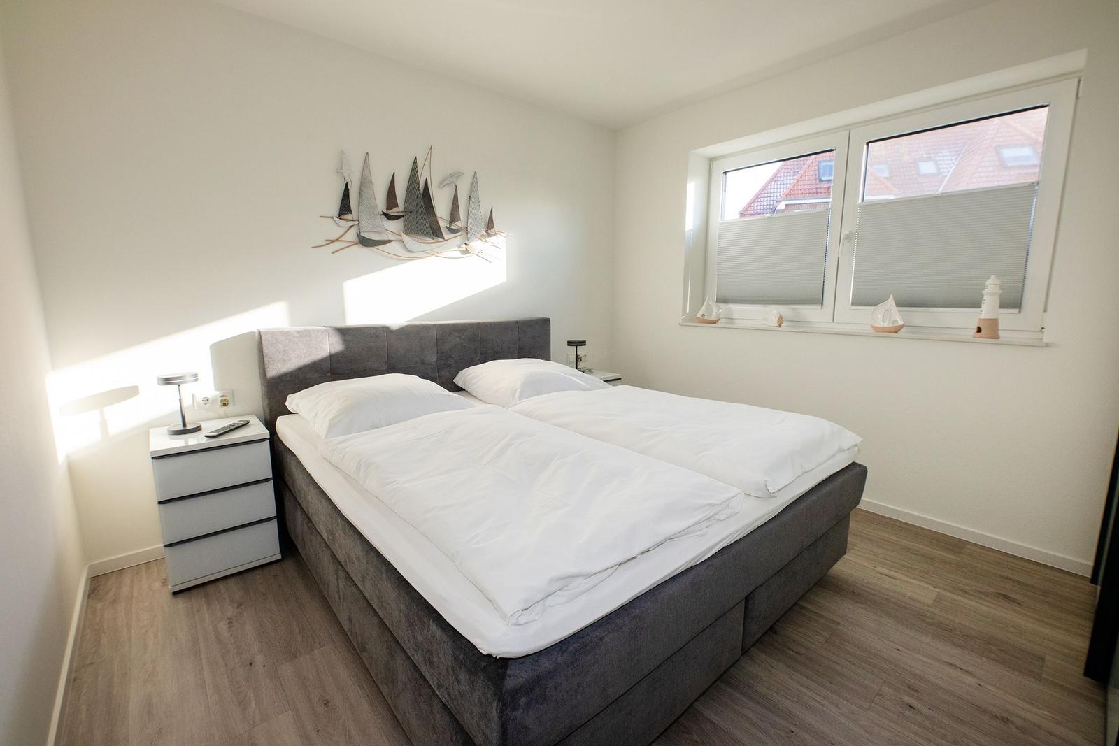 Schlafzimmer mit Doppelbett, Nachttisch und Fenster mit Blick auf Dächer.