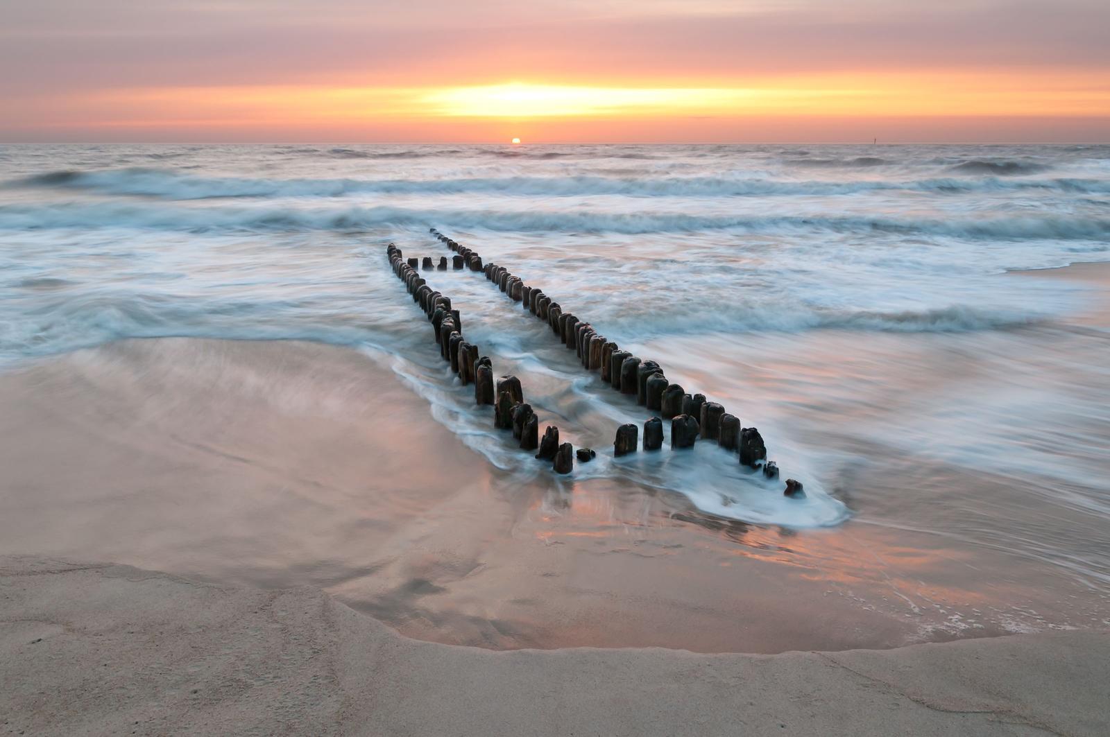 Sunset over the sea with wooden posts in the foreground.