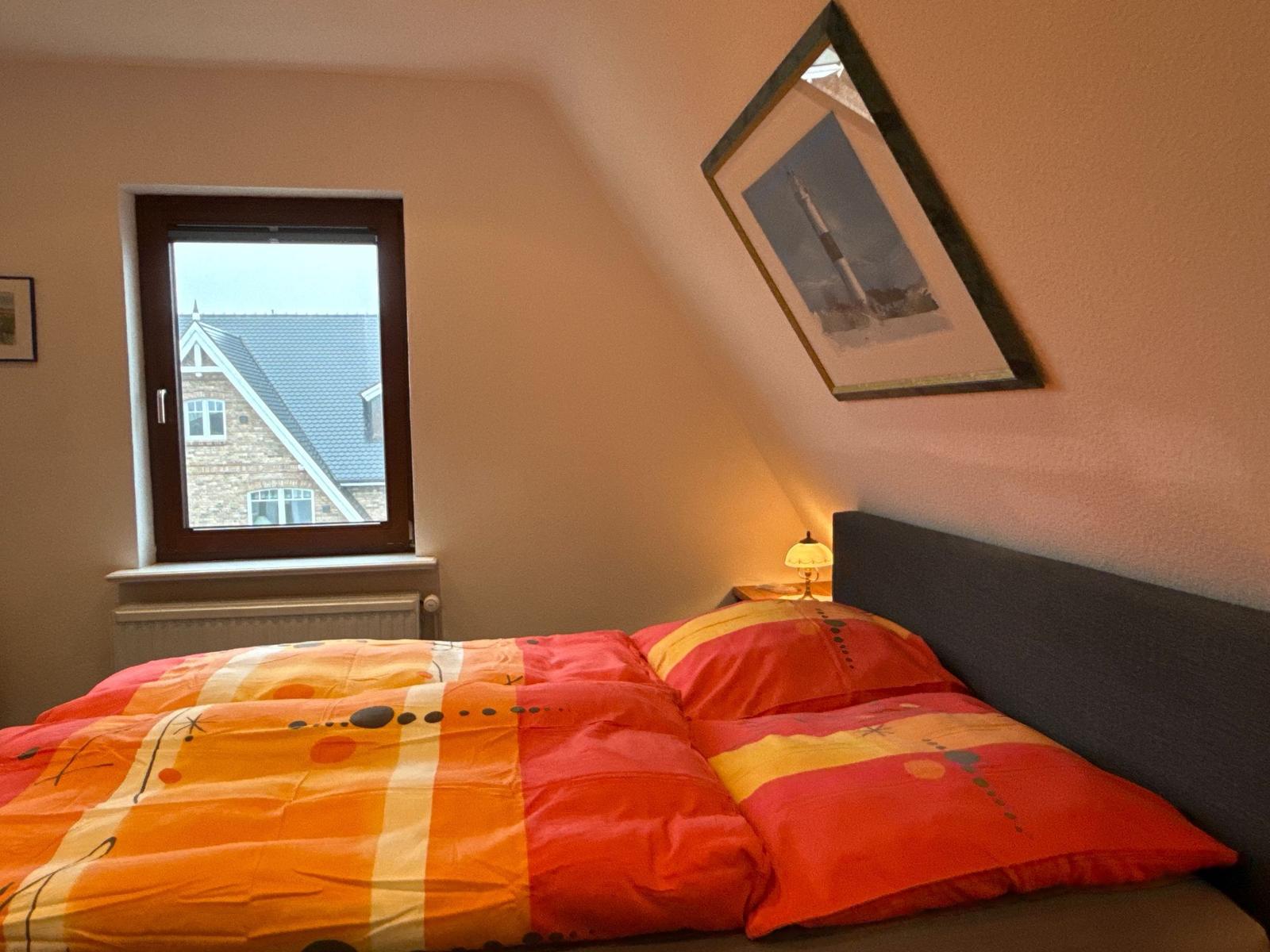 Schlafzimmer mit Bett, Fenster und Wandbild.