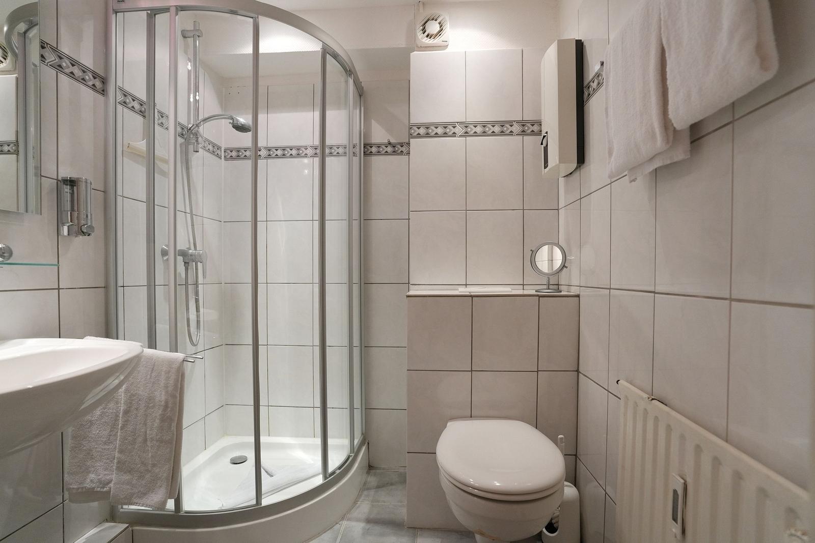 Badezimmer mit Dusche, Toilette und Waschbecken. Fliesenwand mit Muster.
