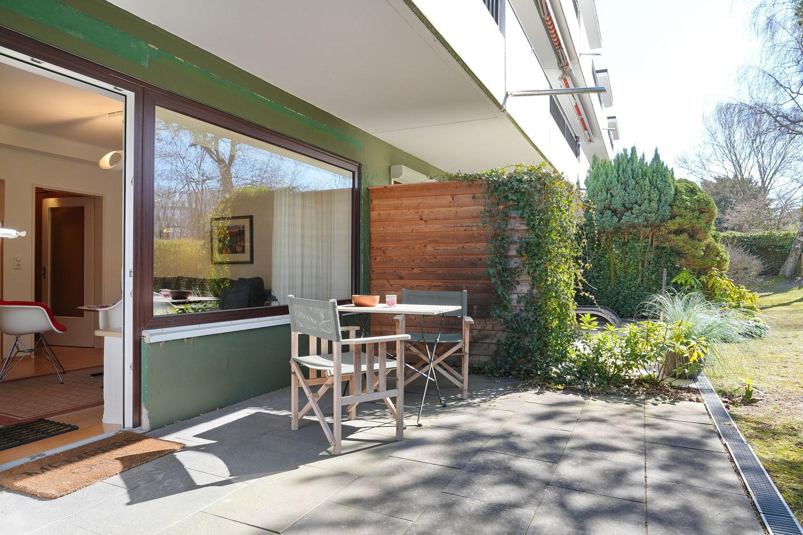 Terrasse mit Tisch und Stühlen, grüne Wand und Pflanzen im Hintergrund.