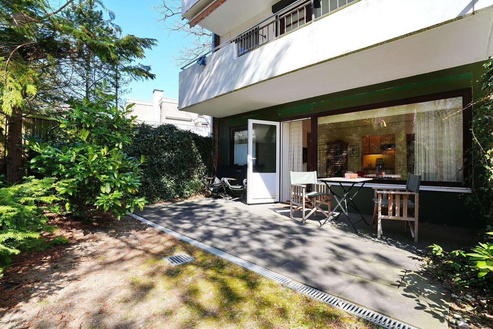 Terrasse mit Tisch und Stühlen, angrenzender Garten mit Bäumen und Sträuchern.