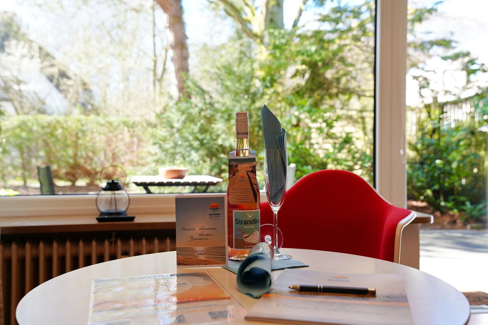 Tisch mit Flasche, Gläser und Willkommenskarte vor Fenster mit Blick auf Garten.