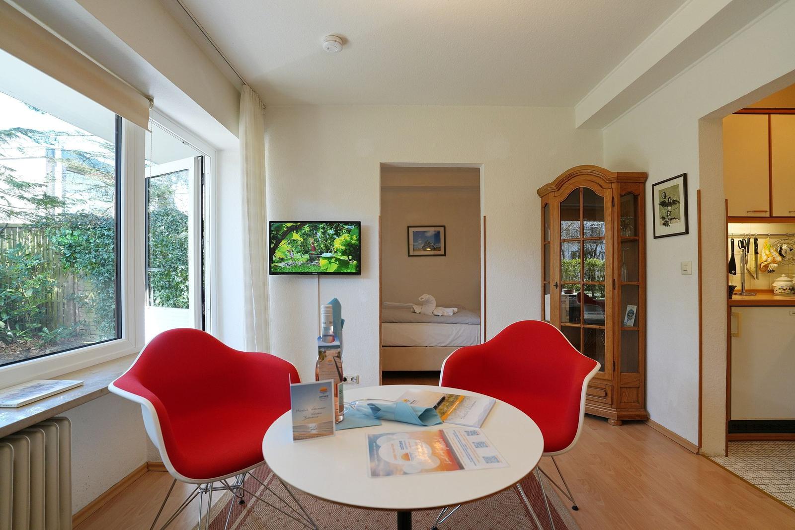 Zimmer mit roten Stühlen, Tisch und Fernseher. Durchgang zur Schlafzimmer und Küche.