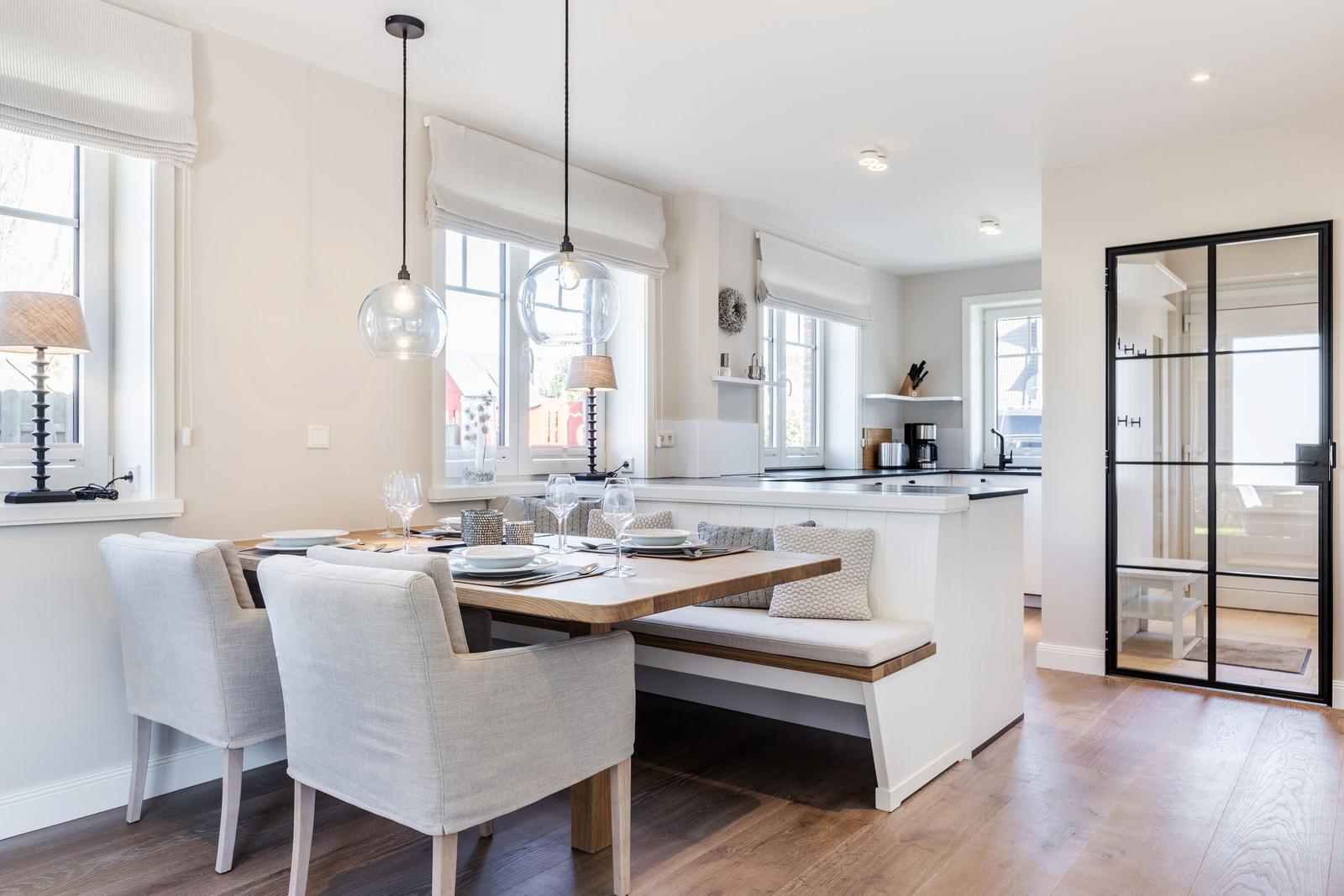 Dining area with table, chairs, and kitchen island. Wooden floor and large windows.