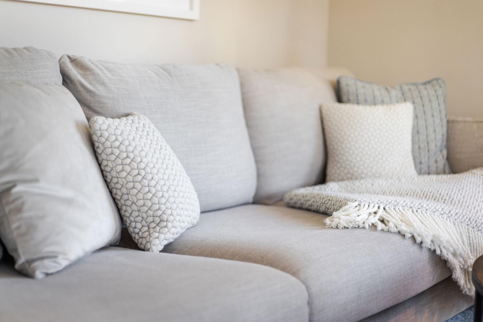 A gray sofa with pillows and a blanket.