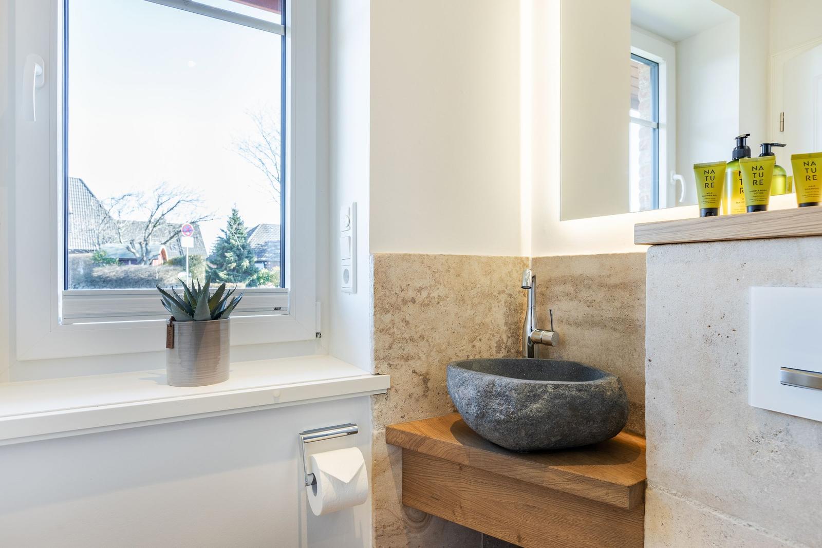 Bathroom with stone basin, wooden vanity, and window view of outdoor area.