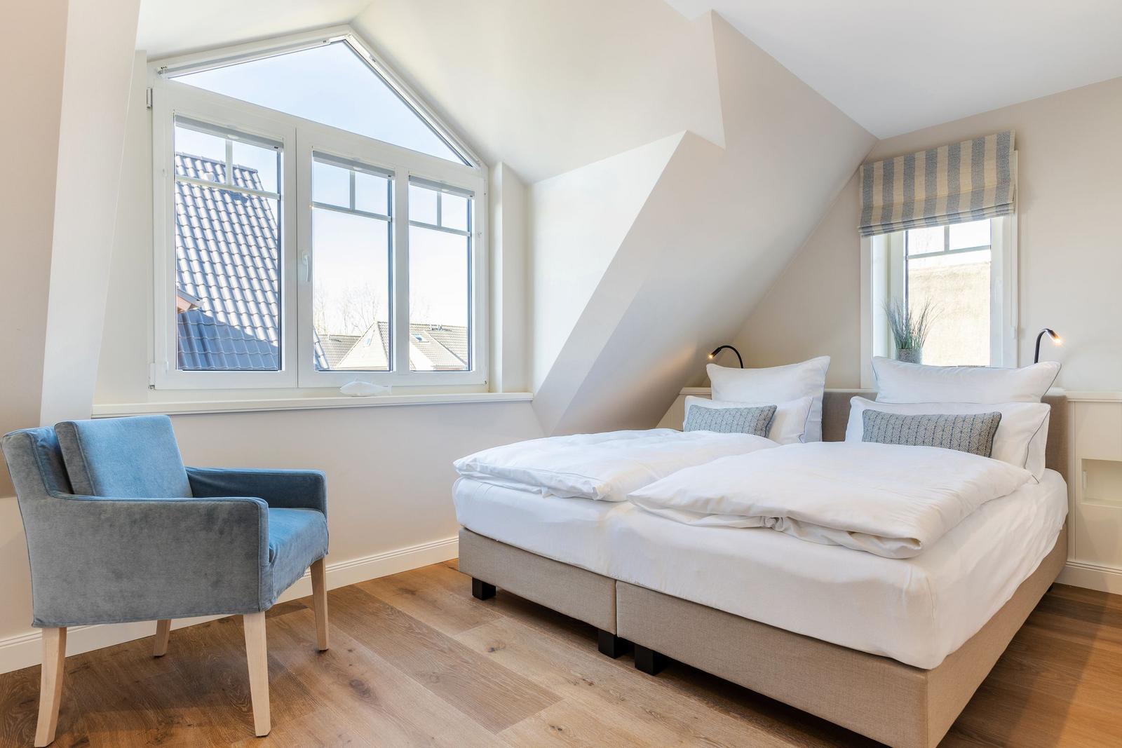 Bedroom with double bed, blue armchair, and large windows.