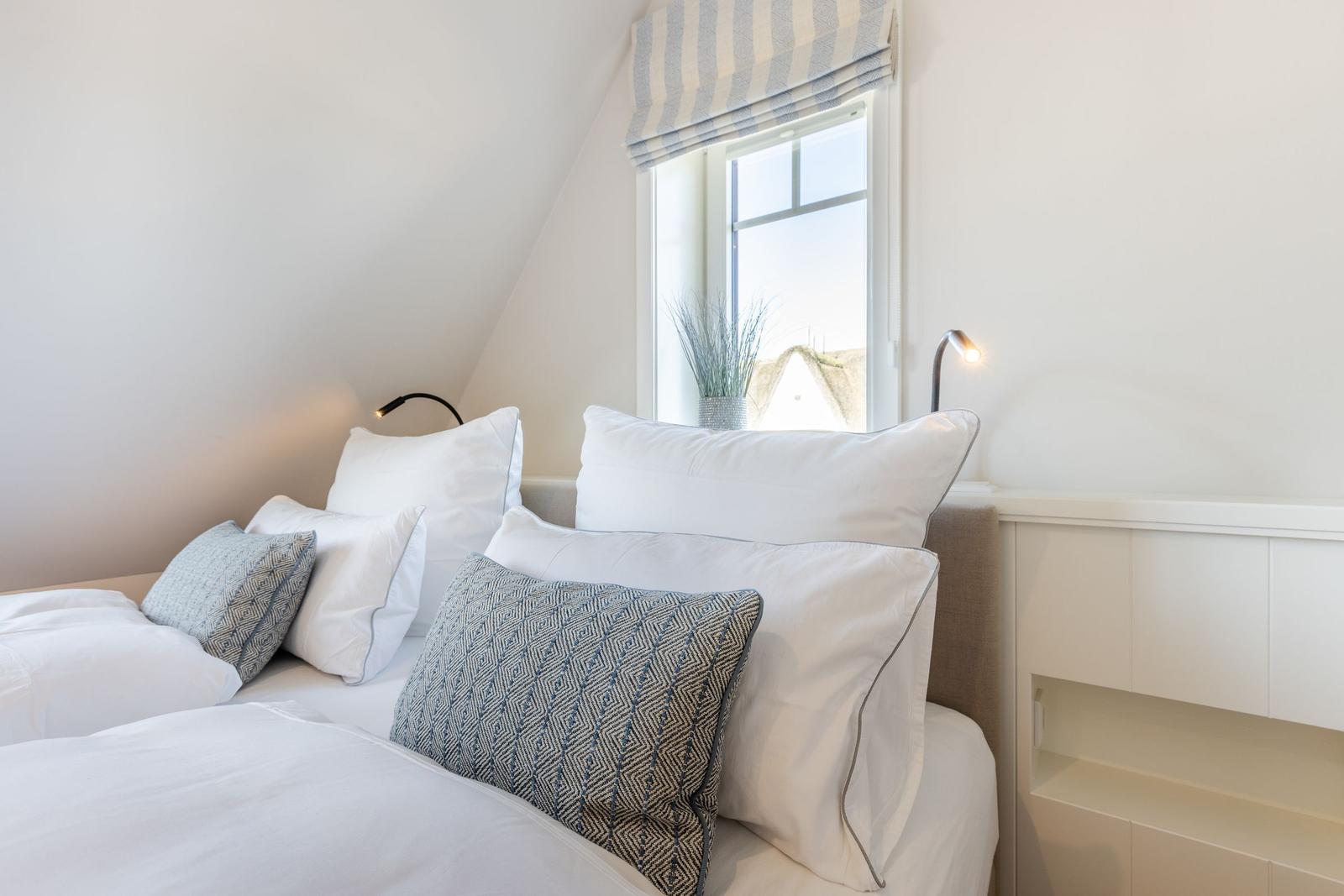 Bedroom with sloped ceiling, window, and bed with pillows.