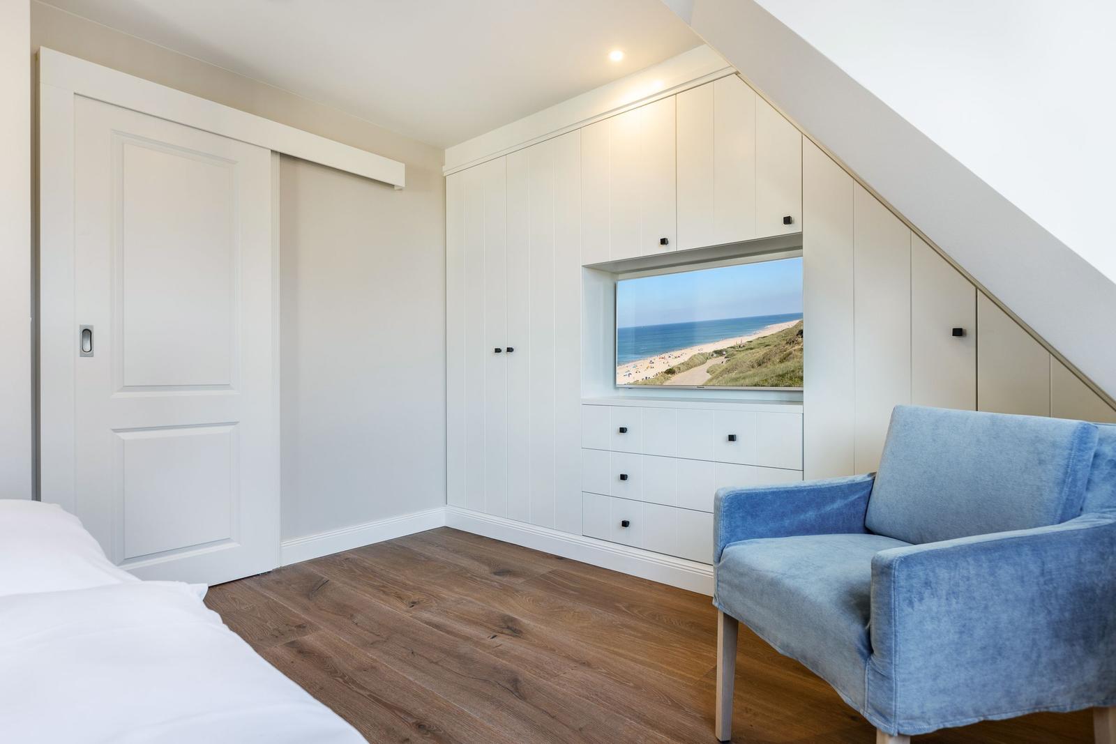 Bedroom with sea view, blue armchair, and white wardrobes.