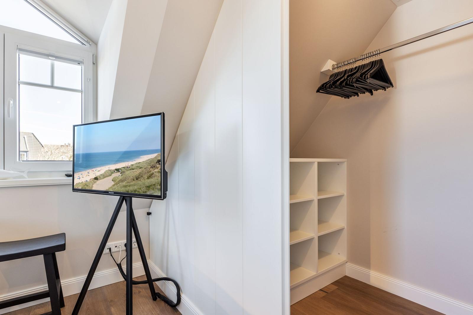 A room with window, TV on stand, and closet with hangers.