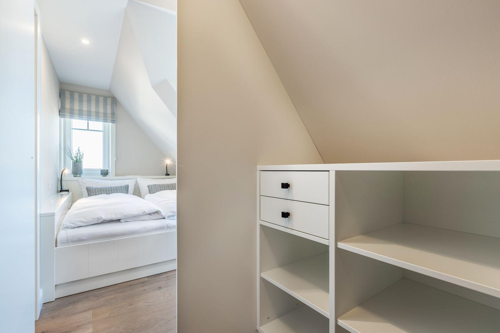 Bedroom with sloped ceiling, white bed, and cabinet with drawers.