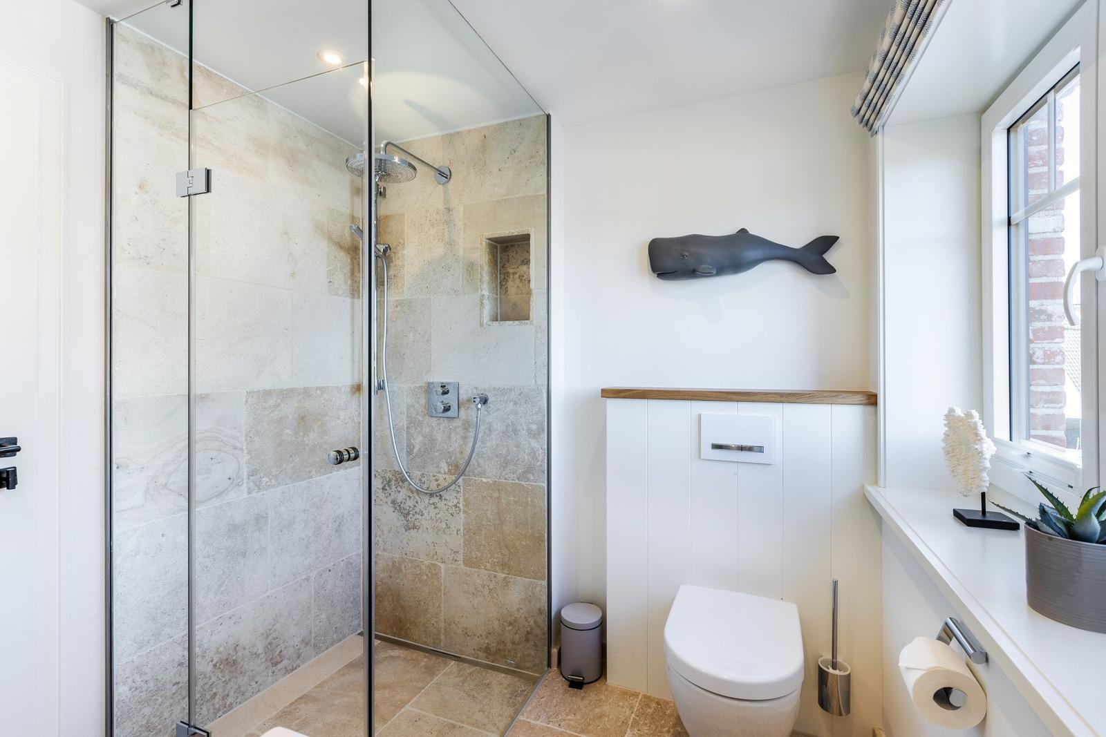 Shower with glass enclosure, toilet, and window with fish decoration.