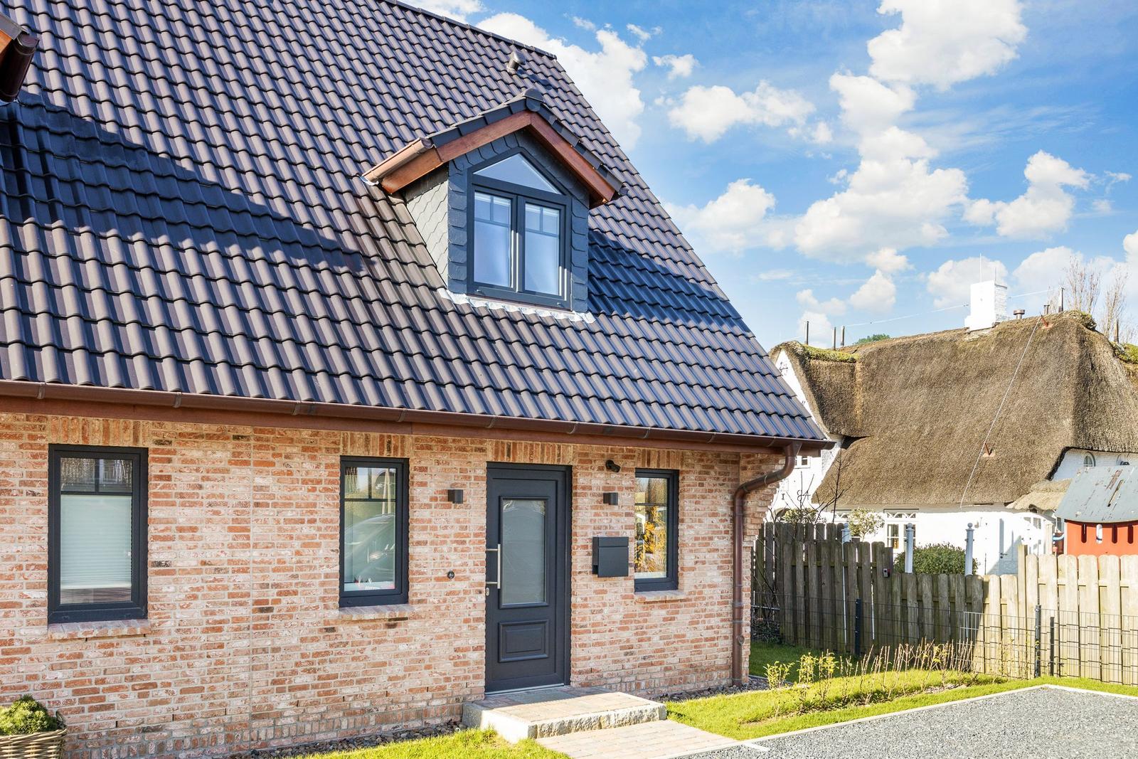 House with brick facade and dark roof, entrance door and windows.