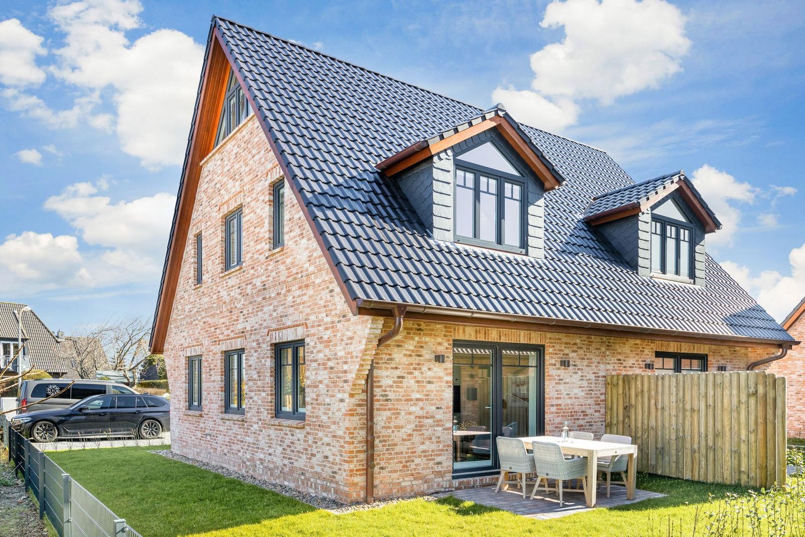 Two-story house with brick facade and dormer windows. Outdoor area with table and chairs.