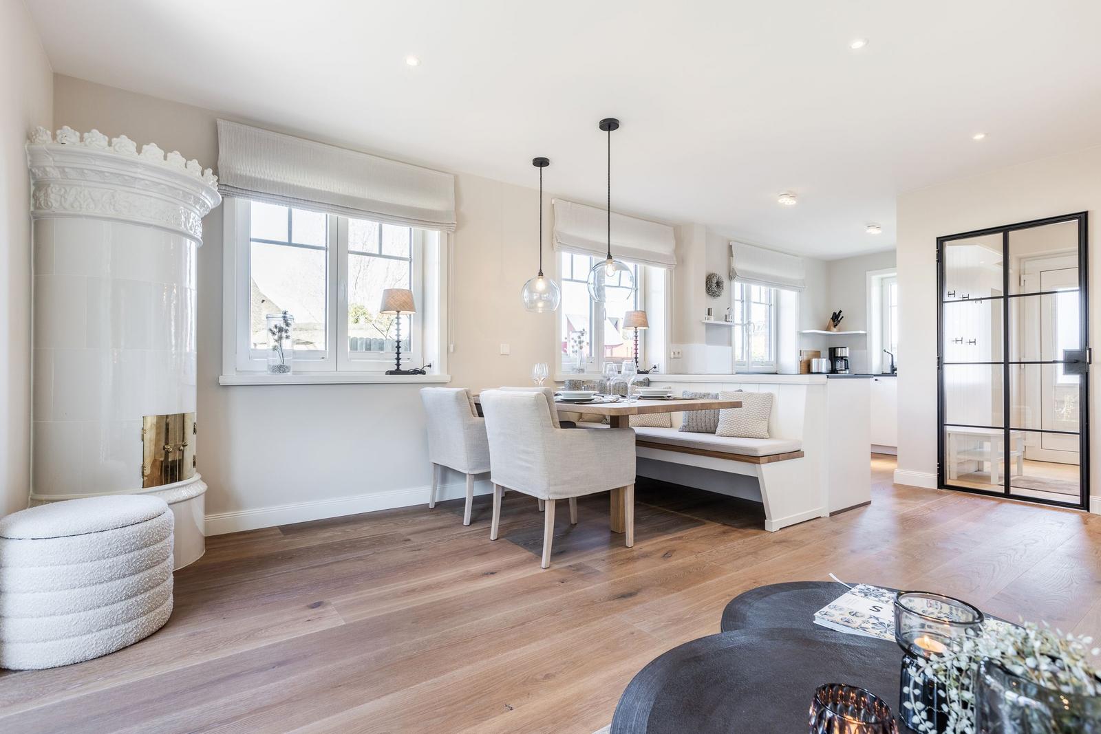 Dining area with table, benches, and windows. White wall and wooden floor.
