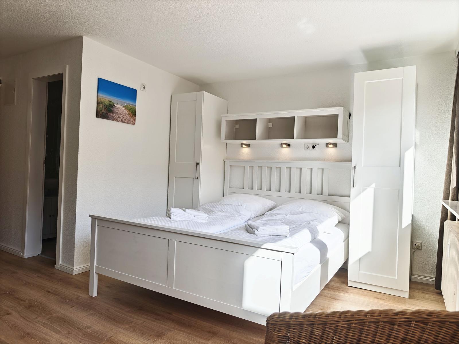 Schlafzimmer mit weißem Bett, Schränken und Wandbild.