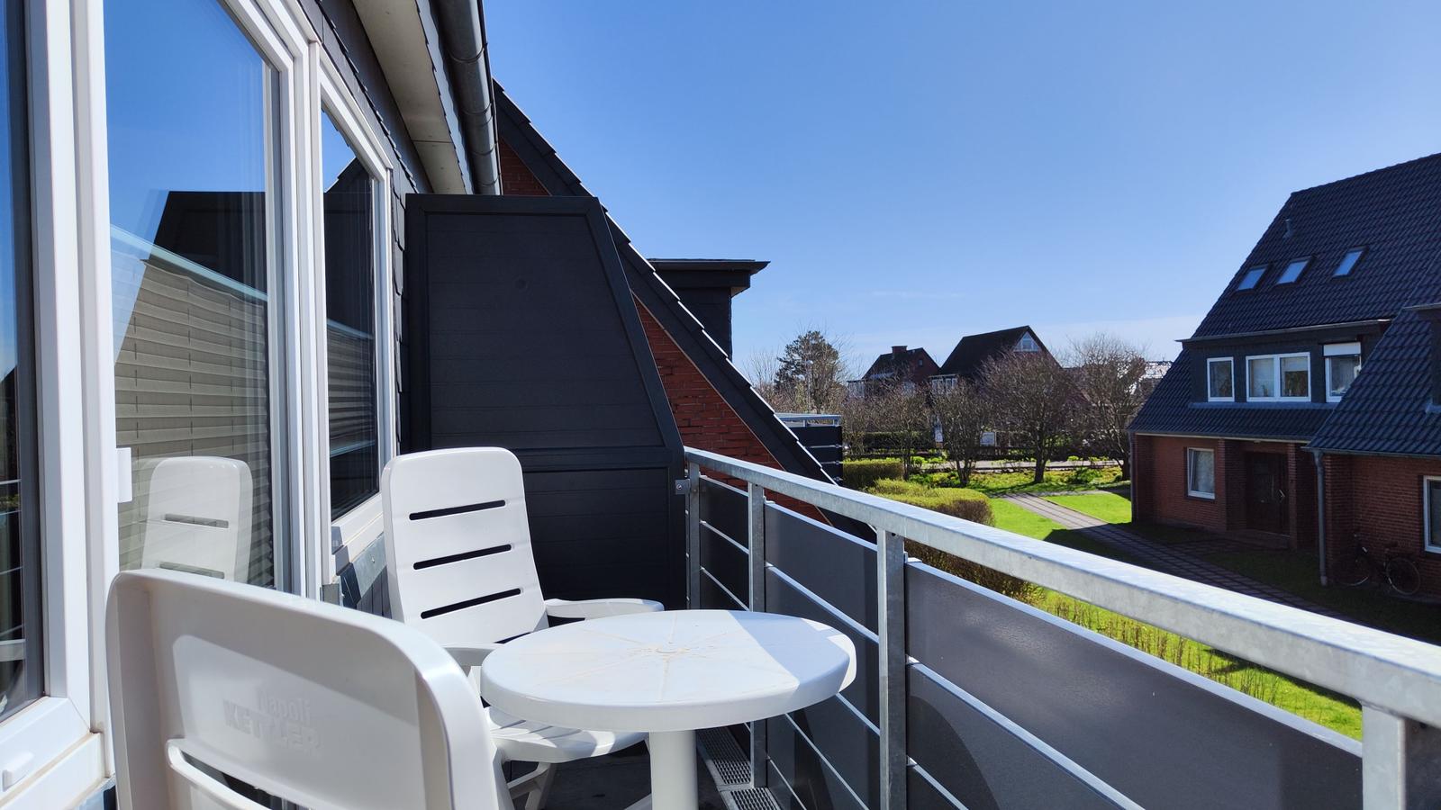 Balkon mit weißem Tisch und Stühlen, Blick auf Wohnhäuser und Grünflächen.