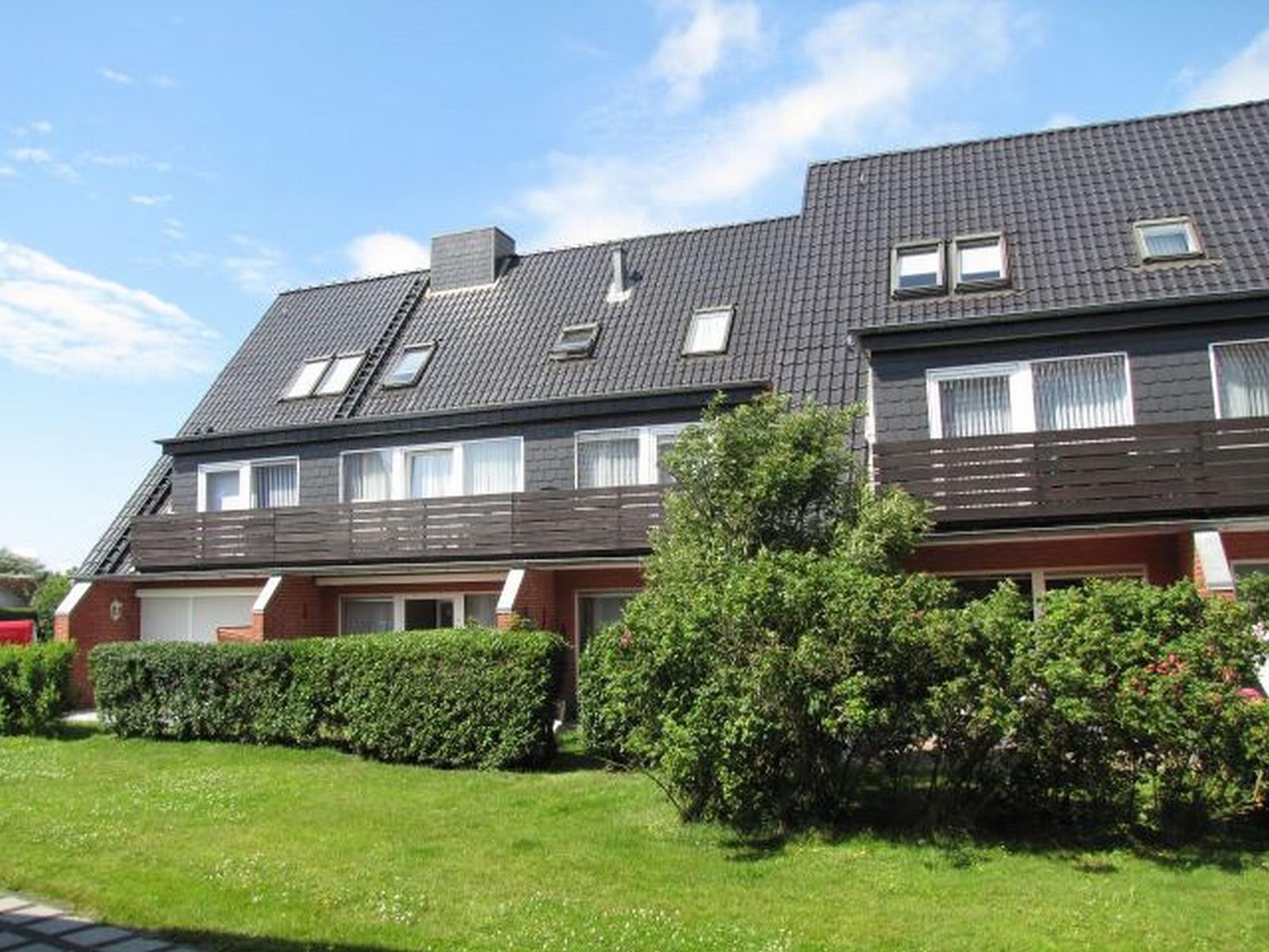 Modernes Mehrfamilienhaus mit Balkonen und Dachfenstern. Grünflächen und Hecken im Vorgarten.