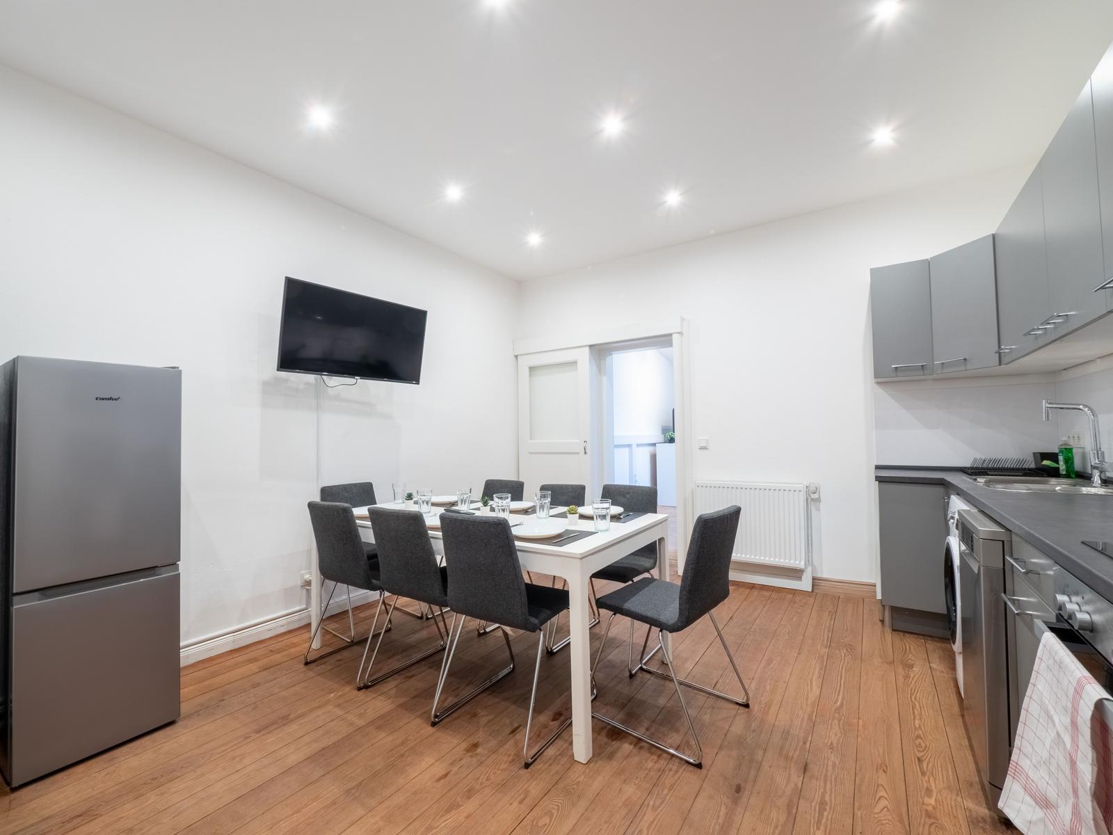 Küche mit Essbereich, Kühlschrank, TV und Holzboden.