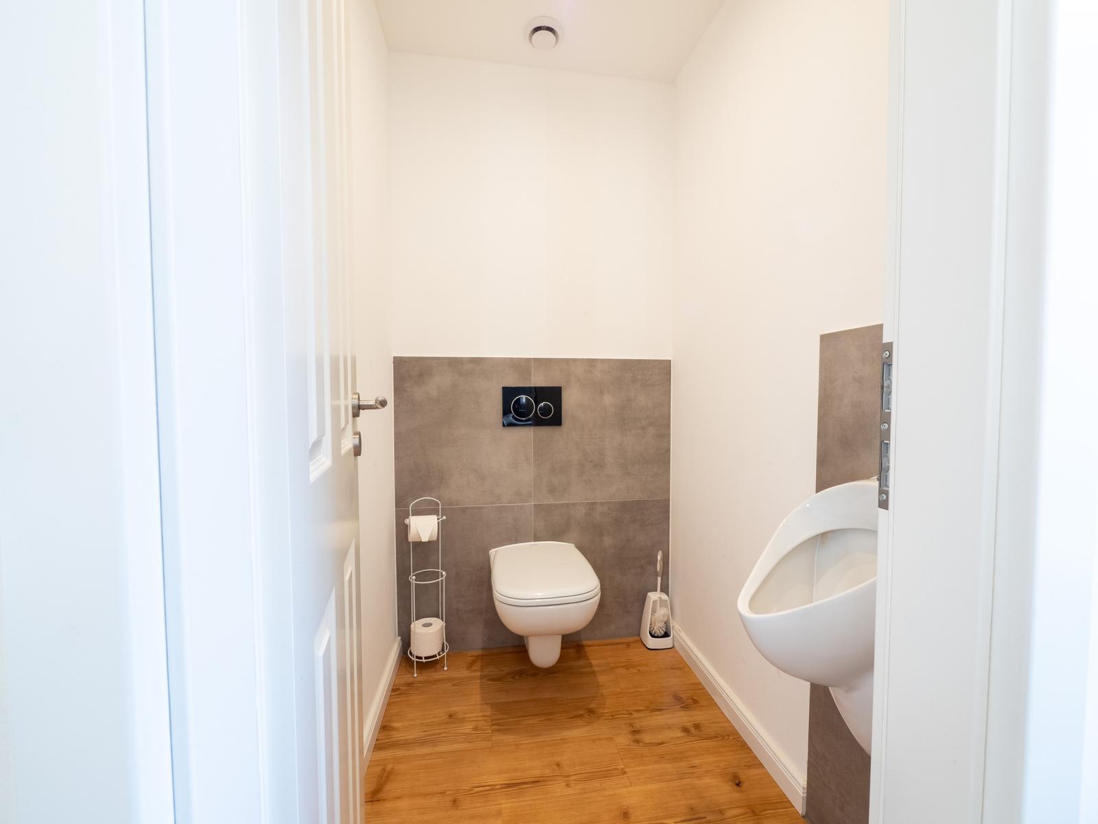 Badezimmer mit Toilette, Urinal und Holzboden