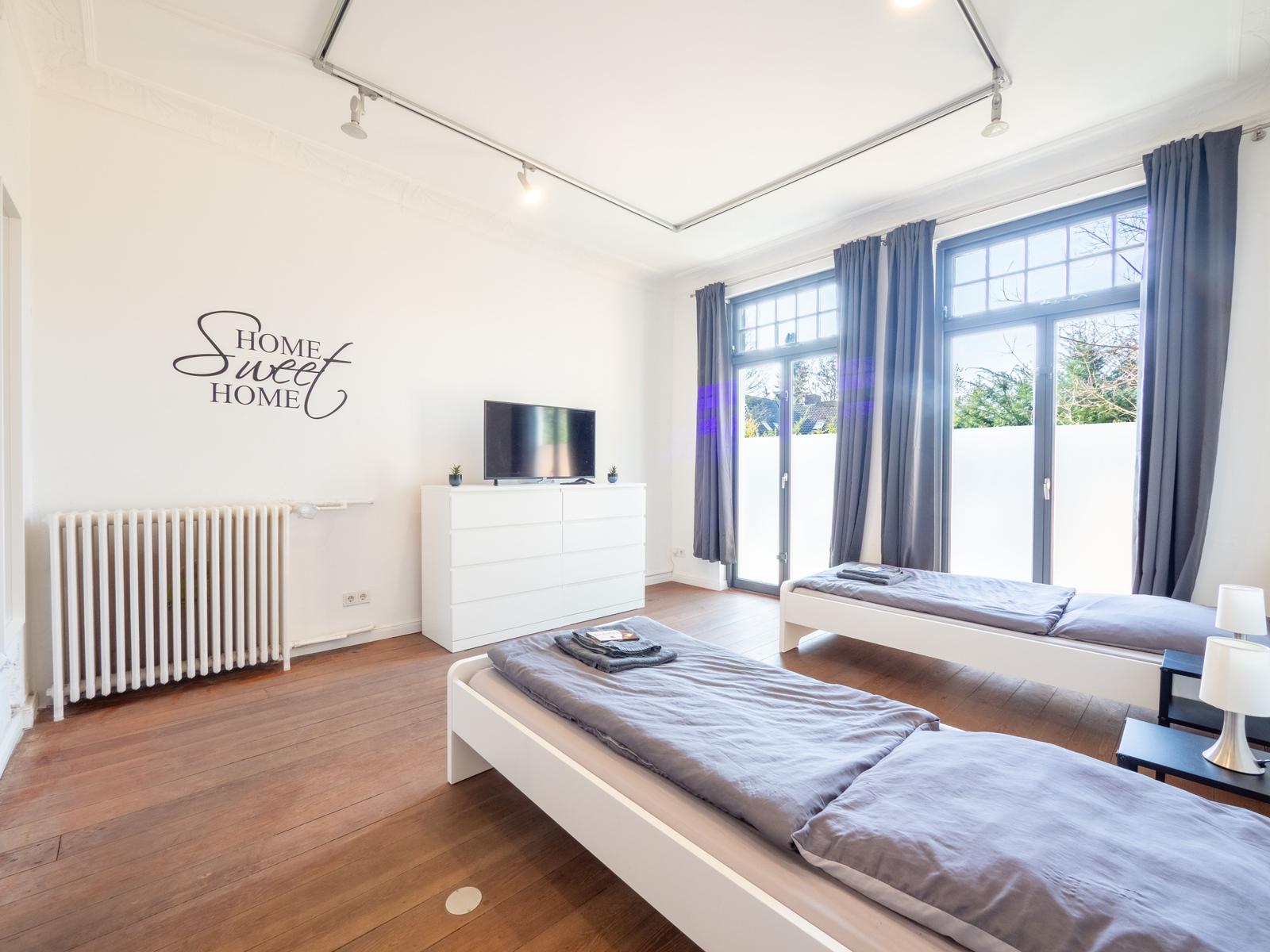 Zwei Betten, Fernseher und große Fenster mit Blick auf Garten.