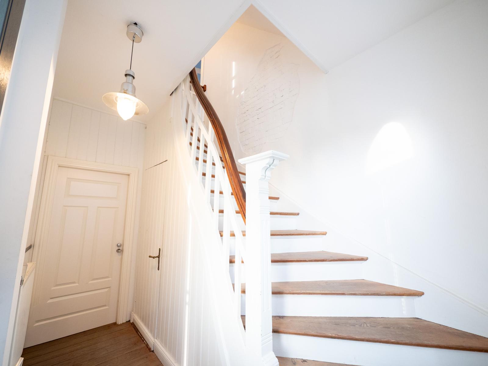 Haus mit Holztreppe und weißer Balustrade. Deckenleuchte und weiße Wände.