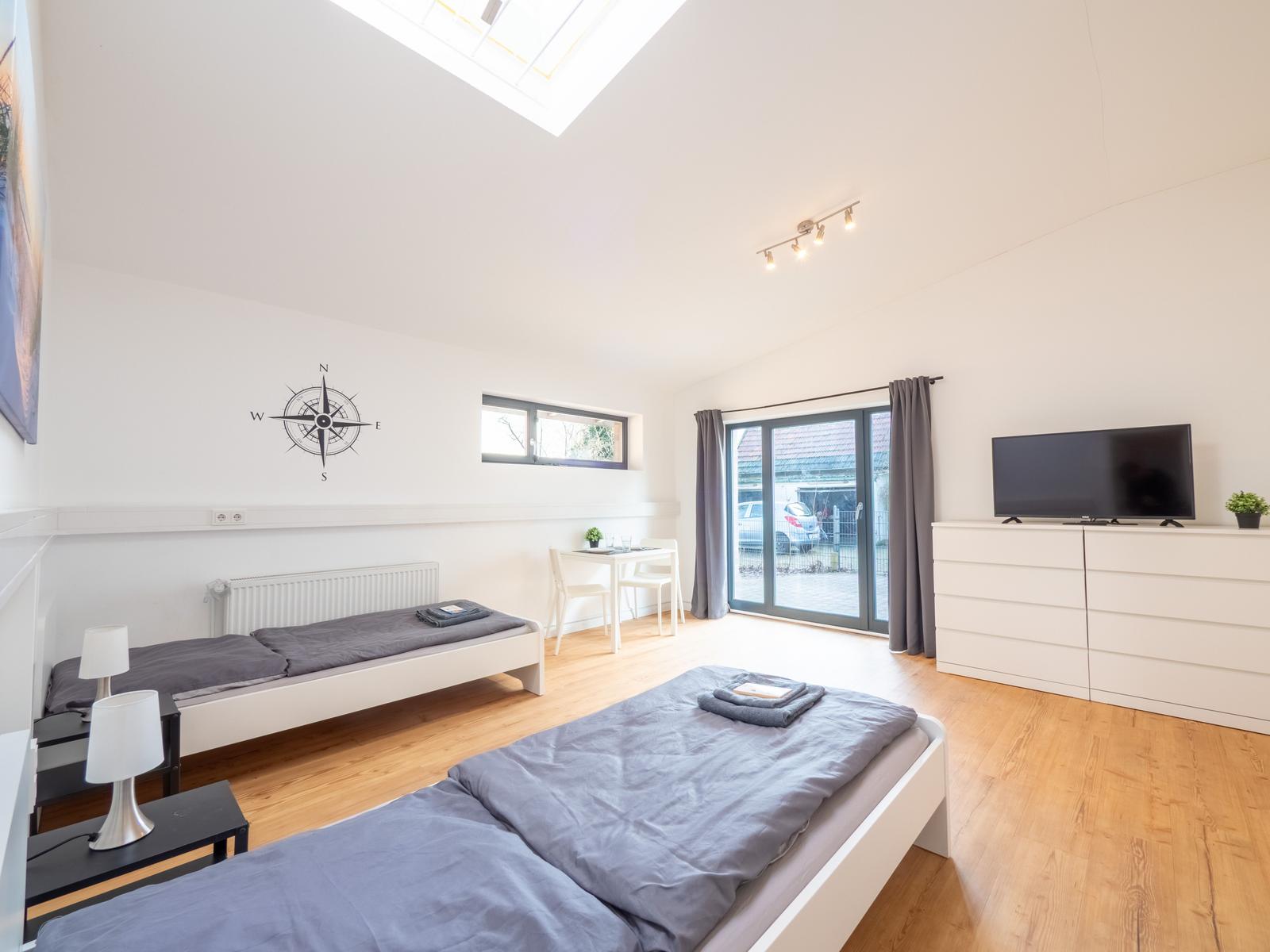Zimmer mit zwei Betten, TV, Schreibtisch und Dachfenster. Blick auf Gartenbereich.