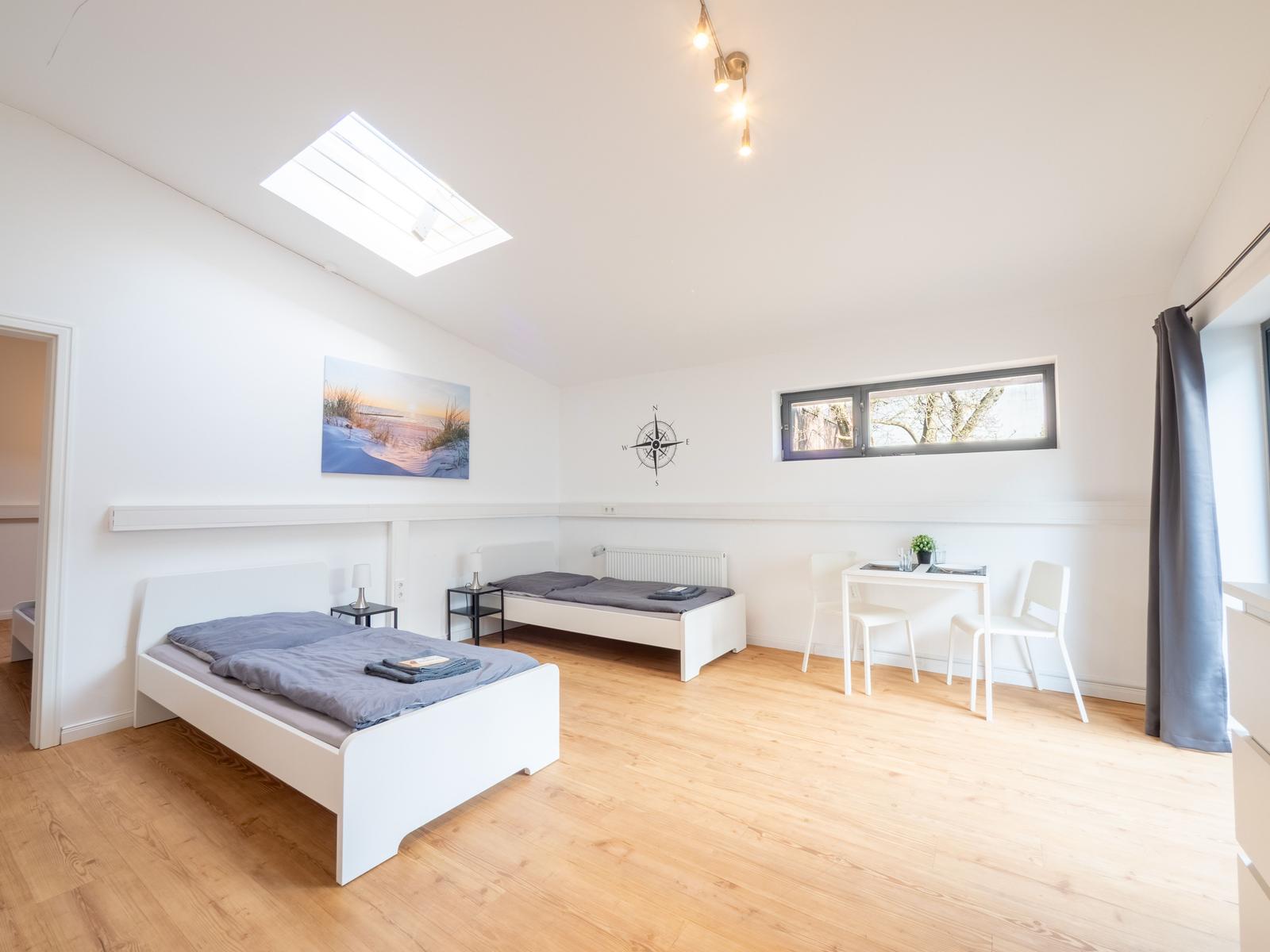 Zimmer mit zwei Betten, Tisch und Fenster. Holzboden und Dachfenster.