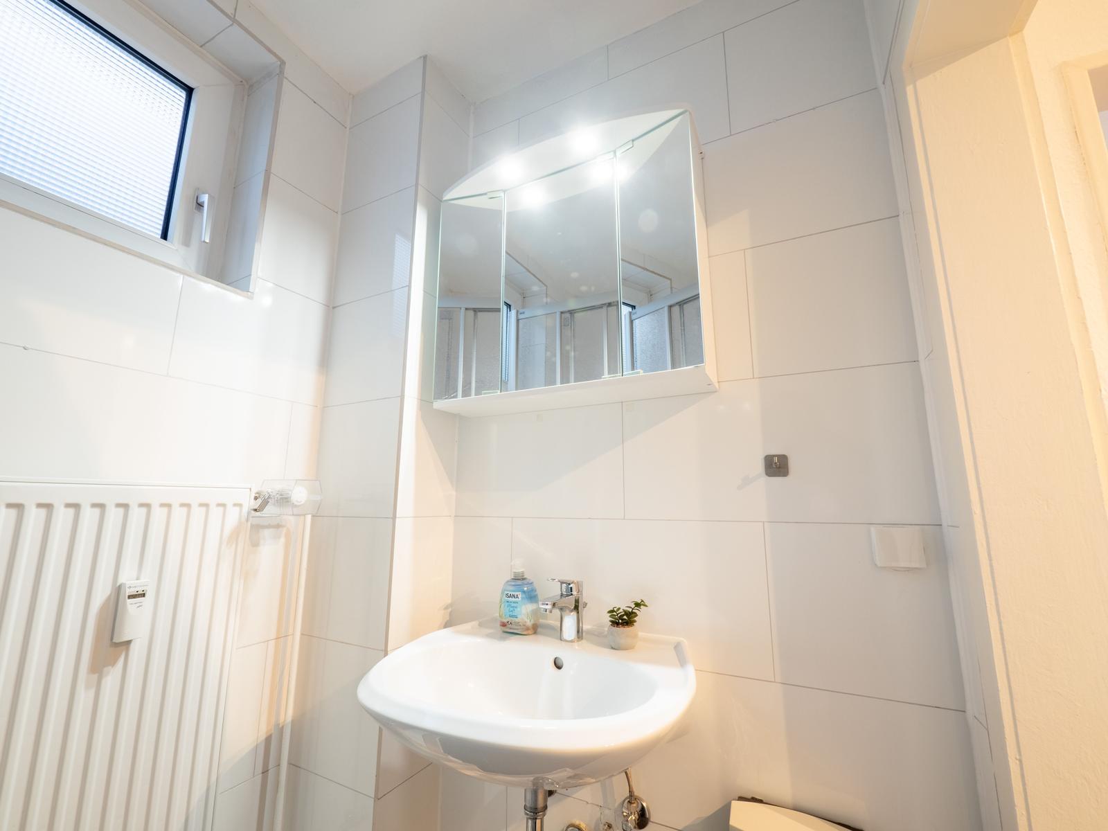 Badezimmer mit Waschbecken, Spiegelschrank und Fenster