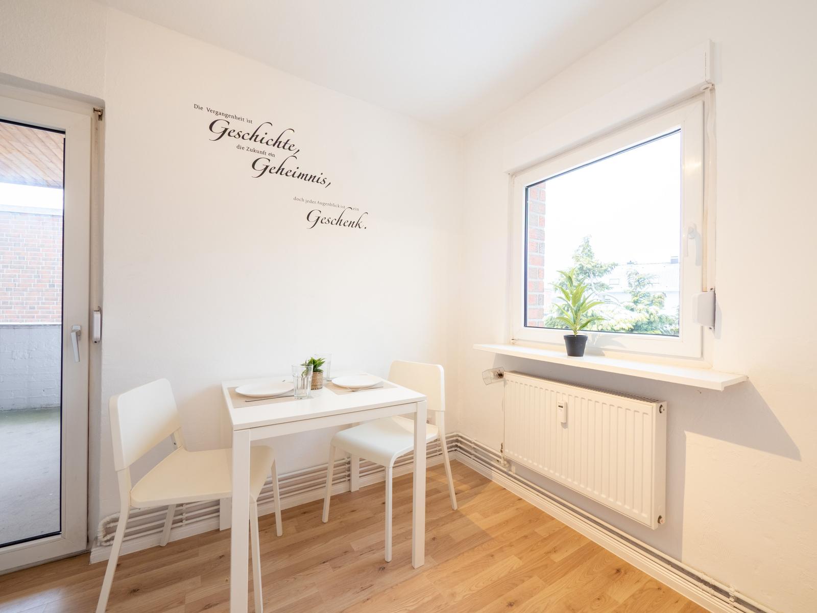 Esszimmer mit weißem Tisch, zwei Stühlen und Fenster mit Pflanze.