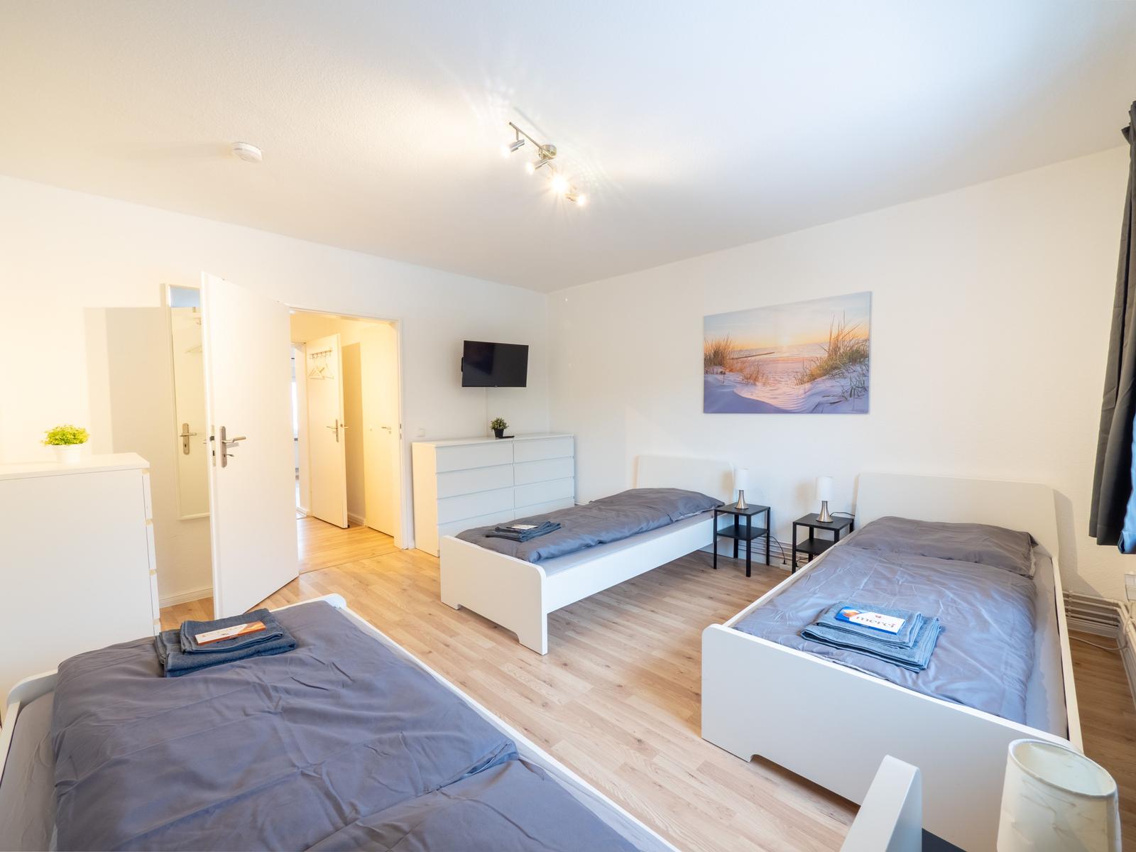 Drei Betten, Fernseher, Kleiderschrank und Wandbild in einem Schlafzimmer.