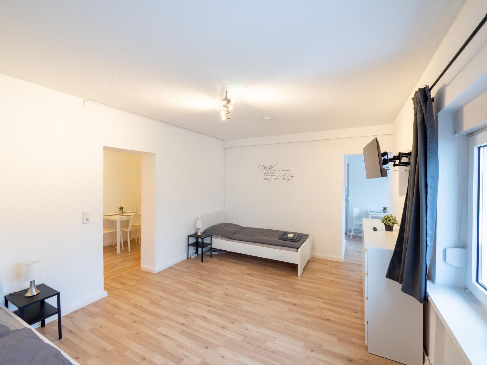 Schlafzimmer mit Bett, Schreibtisch und TV. Durchgang zu Essbereich und Küche.